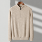 A beige ribbed knit zip-up sweater with a mock neck and long sleeves, hanging on a wooden hanger against a light gray wall with soft diagonal shadows.