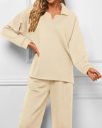 A woman wearing a matching beige knit lounge set with a long-sleeve collared top and wide-leg pants, shown against a light gray paneled wall.