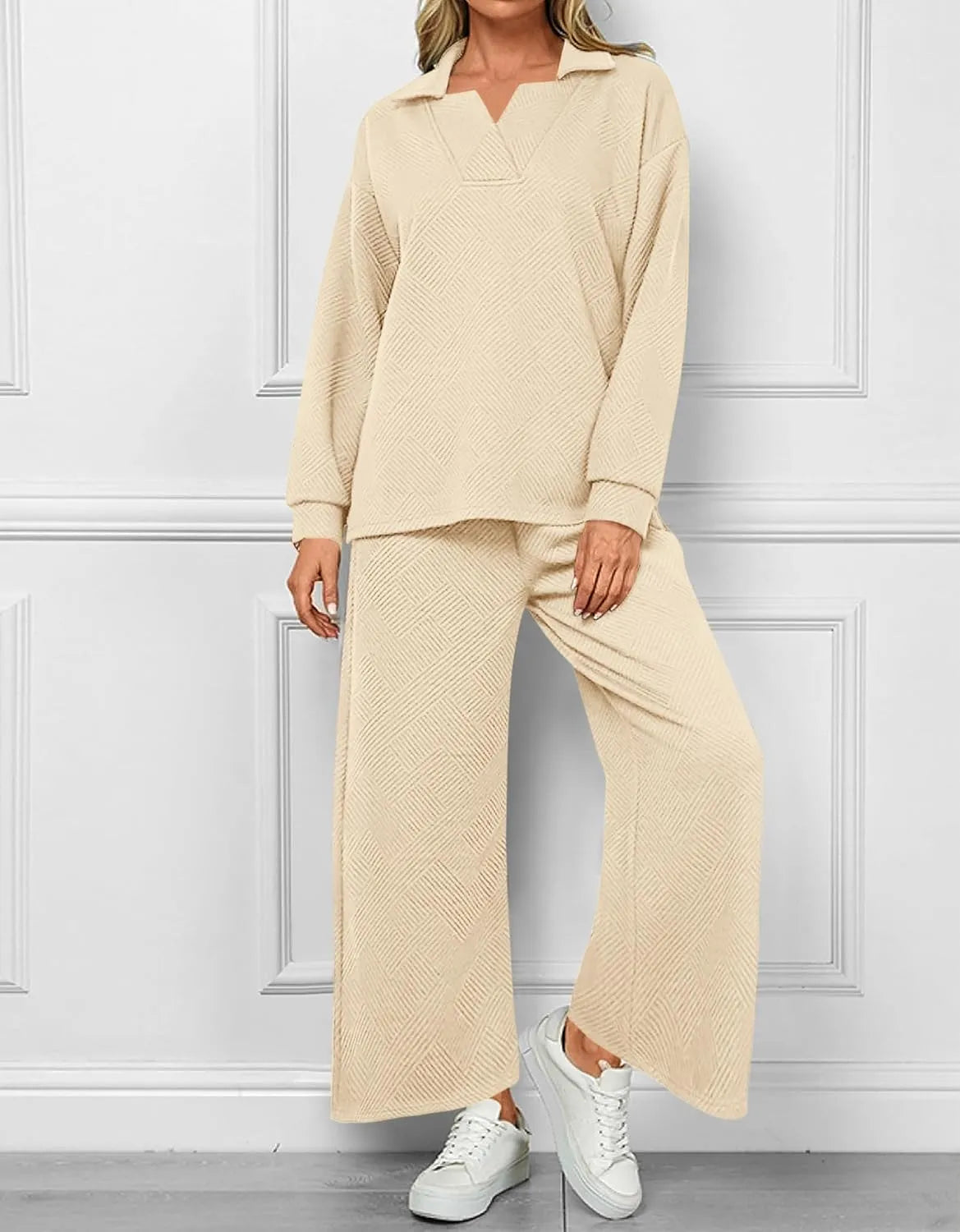 Woman wearing a beige textured outfit with wide-leg pants against a white paneled wall.