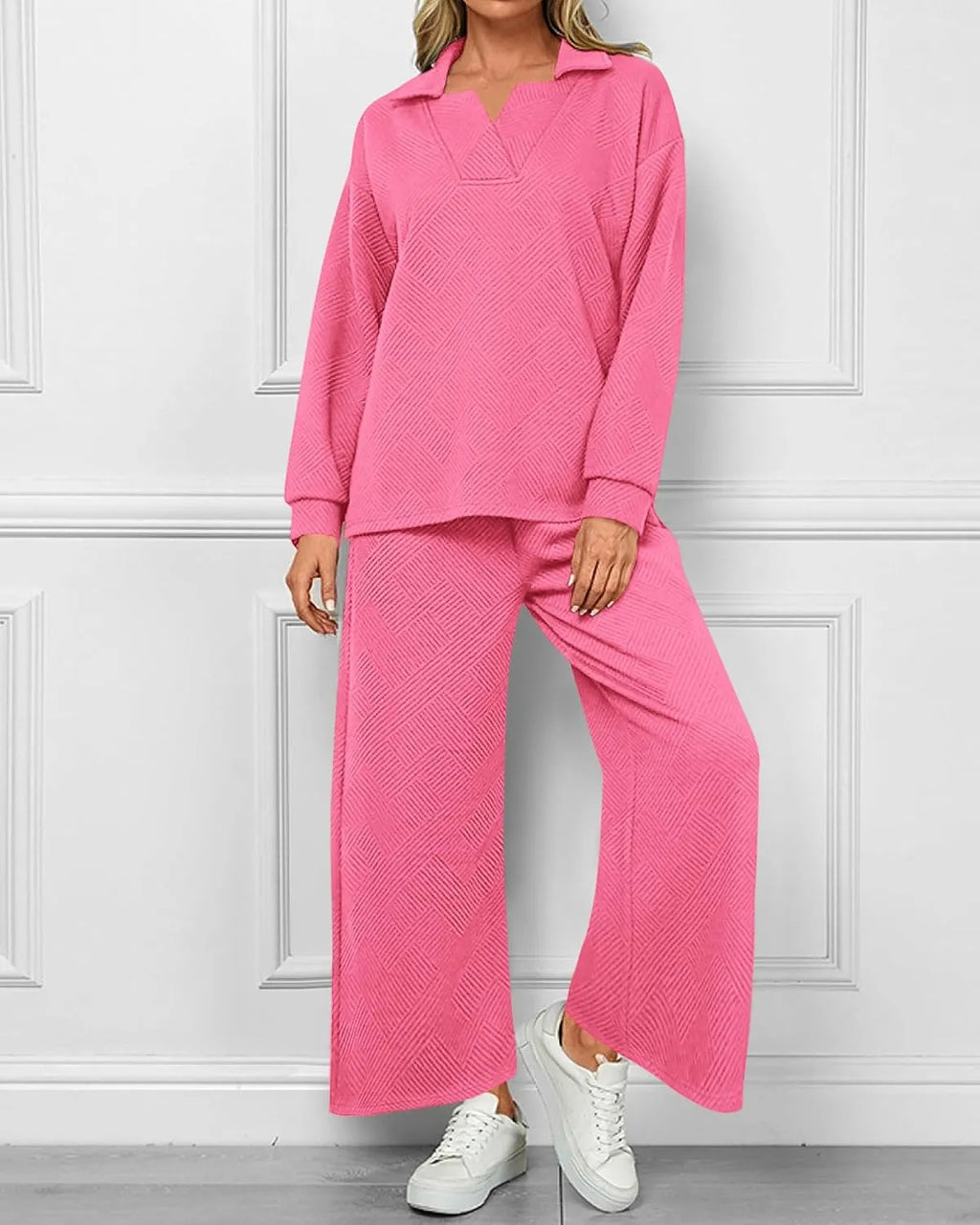Person wearing a pink textured outfit with white sneakers against a white paneled wall.