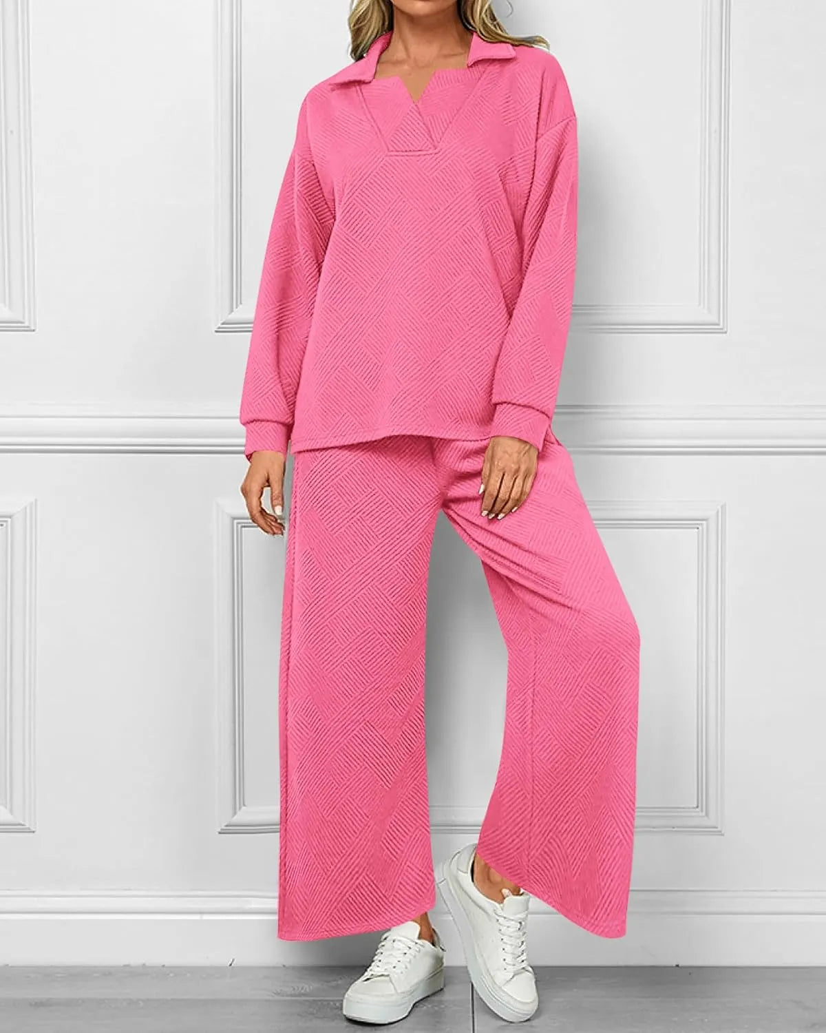 Person wearing a pink textured outfit with white sneakers against a white paneled wall.