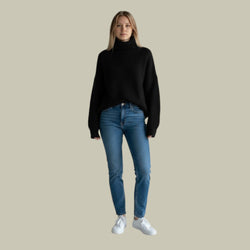 Woman wearing a black sweater and blue jeans on a beige background