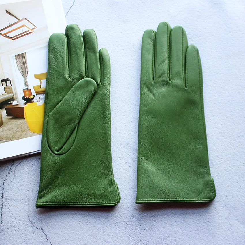Pair of green leather gloves on a textured surface with a magazine in the background.