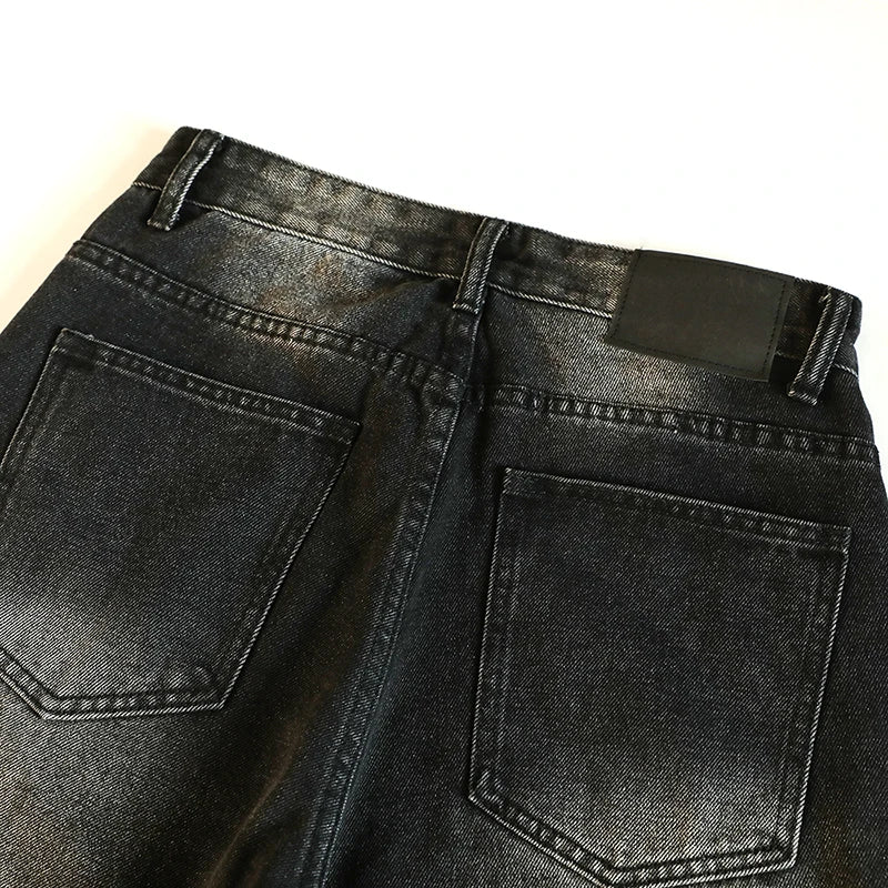 Close-up of black denim jeans with visible wear on a light background
