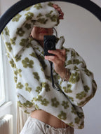 Person wrapped in a white blanket with green floral patterns, holding a camera.