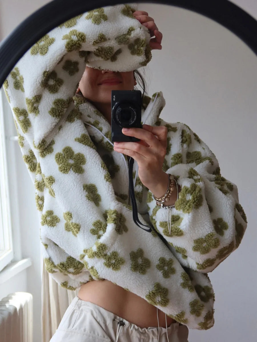 Person wrapped in a white blanket with green floral patterns, holding a camera.