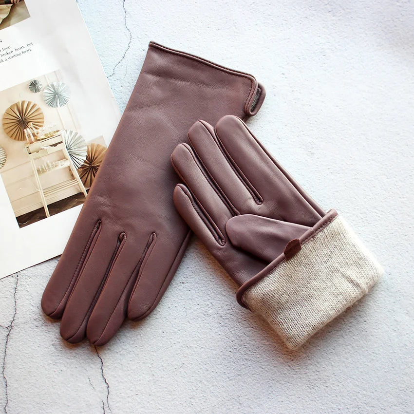 Pair of brown leather gloves with beige lining on a textured surface