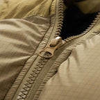 Close-up of a beige quilted jacket with a textured zipper and pull tab, featuring Chinese and English text at the bottom about the zipper being durable and easy to push open.