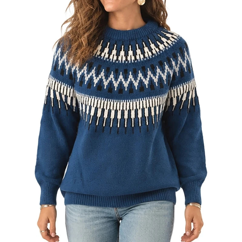 A woman wearing a blue knit sweater with a white and black geometric Fair Isle pattern across the chest and shoulders, paired with light blue jeans against a plain white background.