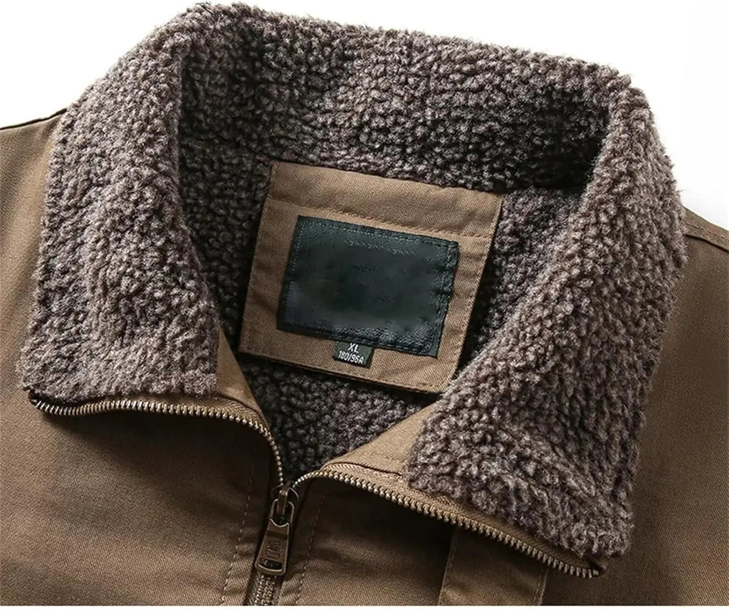 Close-up of a brown jacket with a thick, plush brown sherpa fleece collar and a front zipper, showing a blank brand patch on the inside neck.