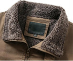 Close-up of a brown jacket with a thick, plush brown sherpa fleece collar and a front zipper, showing a blank brand patch on the inside neck.
