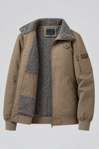 A tan utility-style jacket with a gray speckled sherpa lining, shown on a light gray background. The jacket features a zippered front, a buttoned collar, a chest zip pocket, and a lower zip pocket.