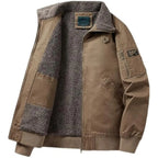 A men's tan utility jacket with a thick gray fleece lining, ribbed knit collar, cuffs, and hem, featuring a front zipper, chest pockets, and a zippered sleeve pocket.