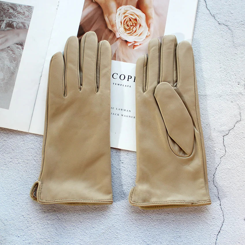 Pair of beige gloves on a textured surface with a magazine in the background.