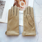 Pair of beige gloves on a textured surface with a magazine in the background.