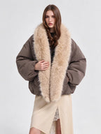 A model wearing a brown puffer jacket with a large beige faux fur collar, styled with a beige wrap skirt against a light gray studio background.