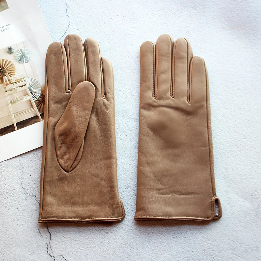 Pair of brown leather gloves on a light gray surface with a magazine in the background.
