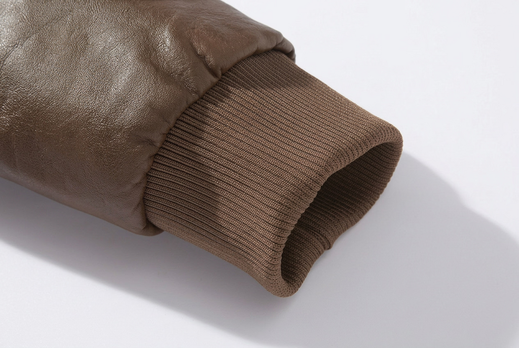 Close-up detail of a brown faux-leather sleeve cuff with a ribbed knit underarm opening, shown on a light gray background.