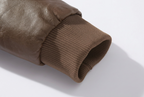 Close-up detail of a brown faux-leather sleeve cuff with a ribbed knit underarm opening, shown on a light gray background.