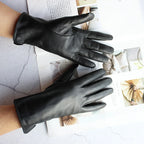 Black leather gloves on a light gray surface with a magazine in the background