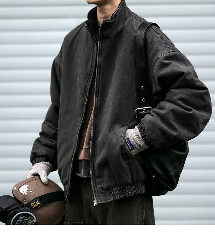 Person wearing a dark jacket holding a helmet against a gray background