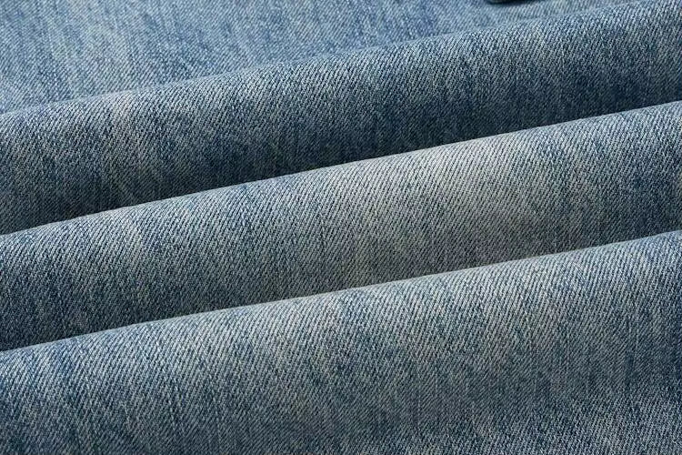 A close-up of blue denim fabric with visible twill texture and soft folds.
