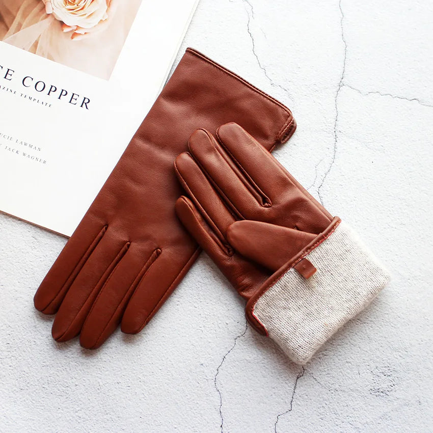 Pair of brown leather gloves with a beige lining on a textured white surface.