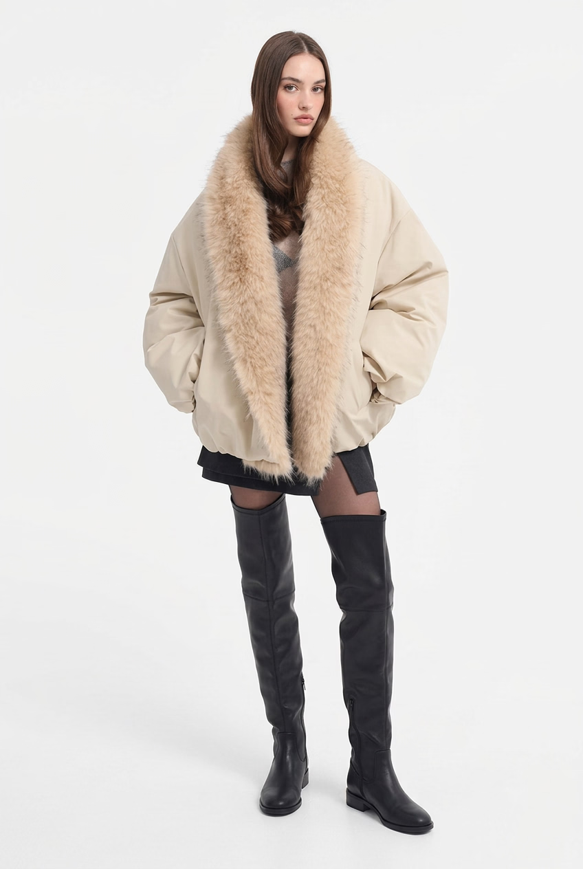 A model wearing a beige puffer jacket with a large, fluffy beige faux-fur collar, styled with a black mini skirt and black knee-high boots against a plain white background.