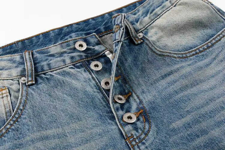 Close-up of a pair of light blue denim jeans showing the button fly, belt loops, and front pocket details.