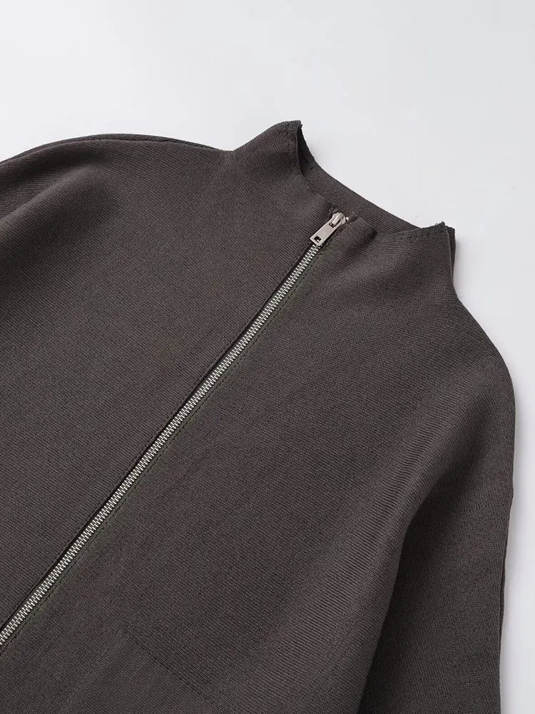 Close-up of a dark brown ribbed knit garment with a silver zipper at the neckline, laid flat on a light gray background.