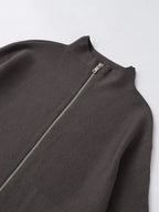 Close-up of a dark brown ribbed knit garment with a silver zipper at the neckline, laid flat on a light gray background.
