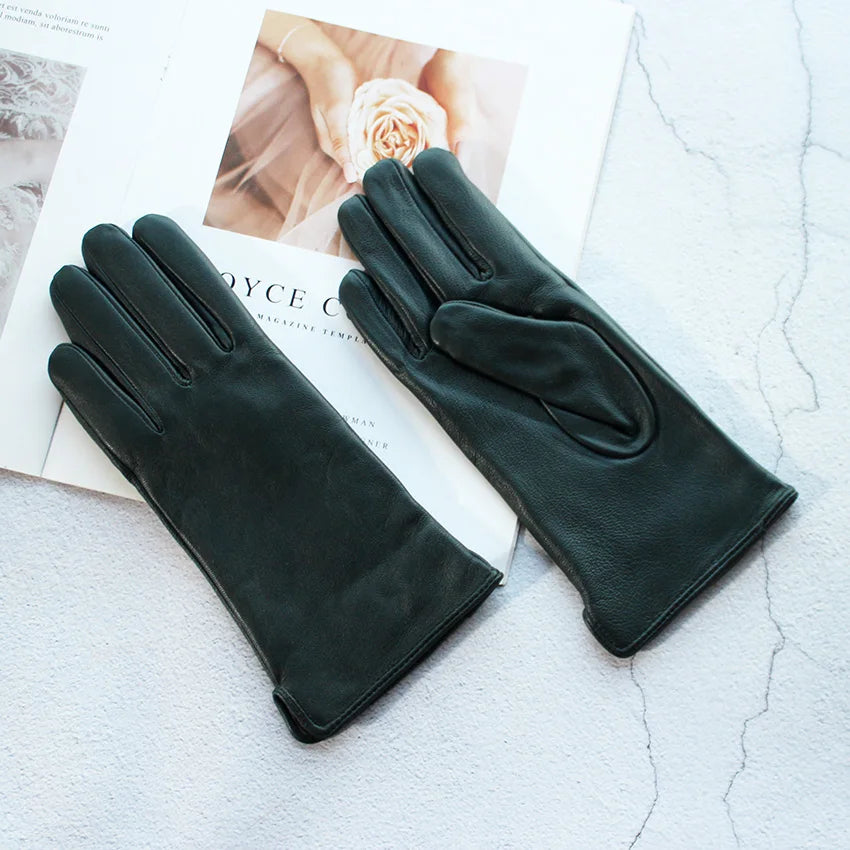 Pair of black leather gloves on a textured surface with a magazine underneath.