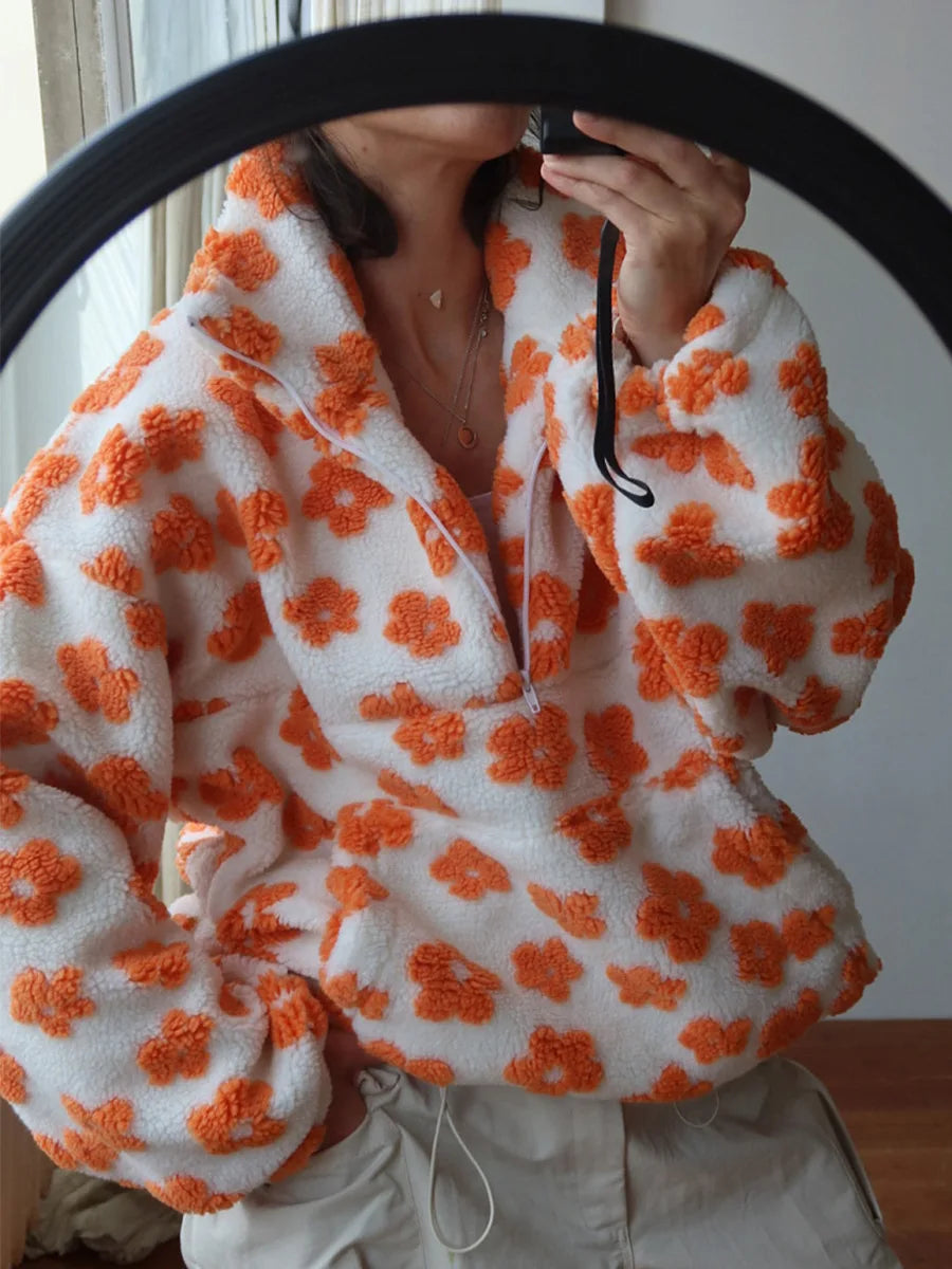A person taking a mirror selfie wearing a fuzzy white quarter-zip pullover with an orange floral pattern, paired with light beige pants.