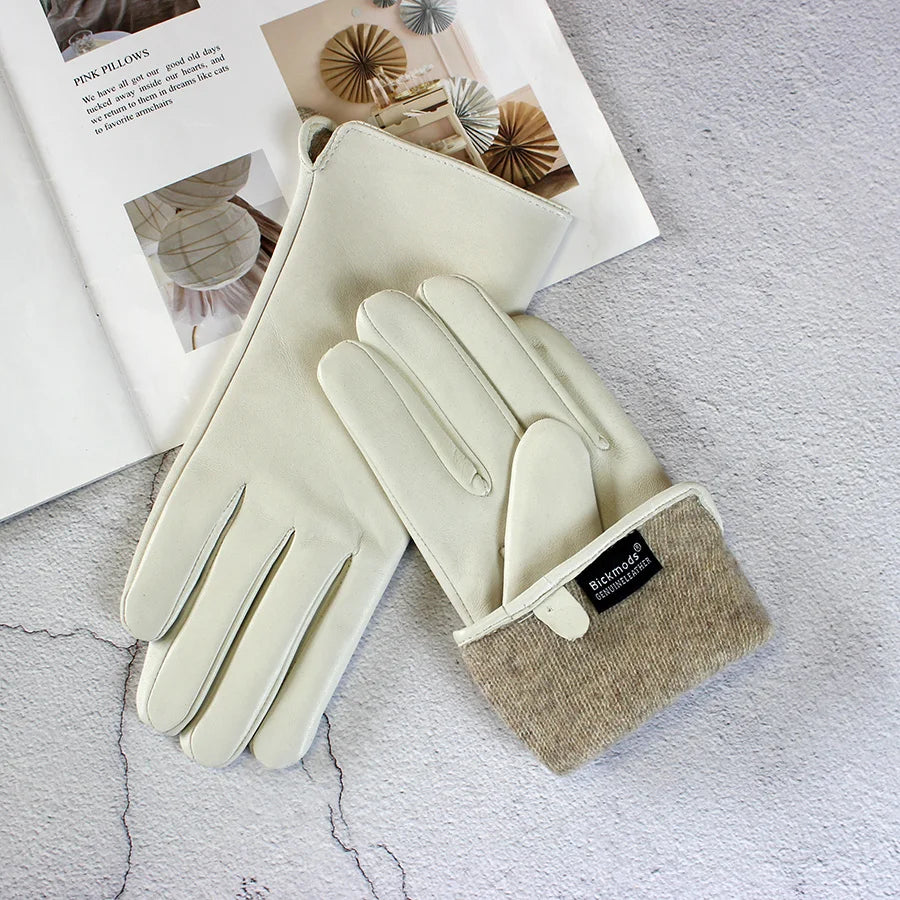 Pair of cream gloves with beige cuffs on a textured surface with a magazine in the background.