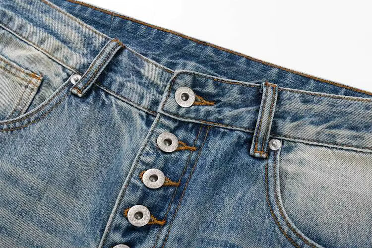 Close-up of a pair of blue denim jeans showing the front button fly, metal buttons, belt loops, and pocket details on a white background.