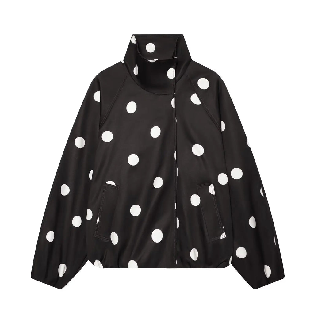 A black zip-up jacket with a high stand-up collar, featuring a bold white polka dot pattern, displayed against a solid white background.
