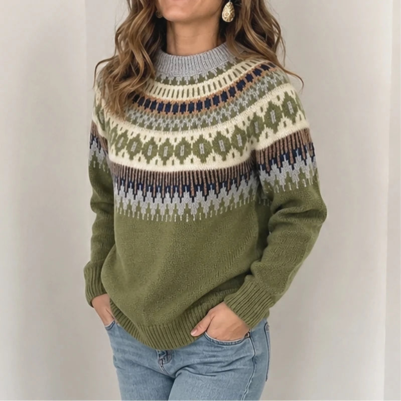 A woman wearing a knit crewneck sweater with a green base and a multicolor Fair Isle pattern across the chest and shoulders, paired with light blue jeans.