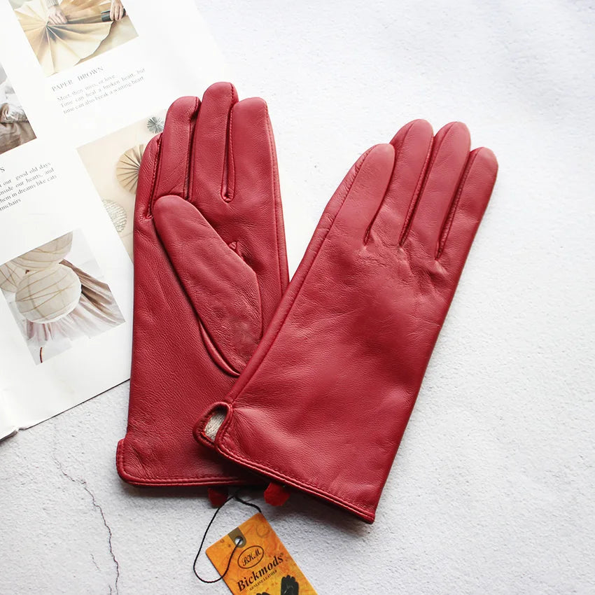 Pair of red leather gloves on a textured surface with a visible brand tag.