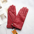 Pair of red leather gloves on a textured surface with a visible brand tag.
