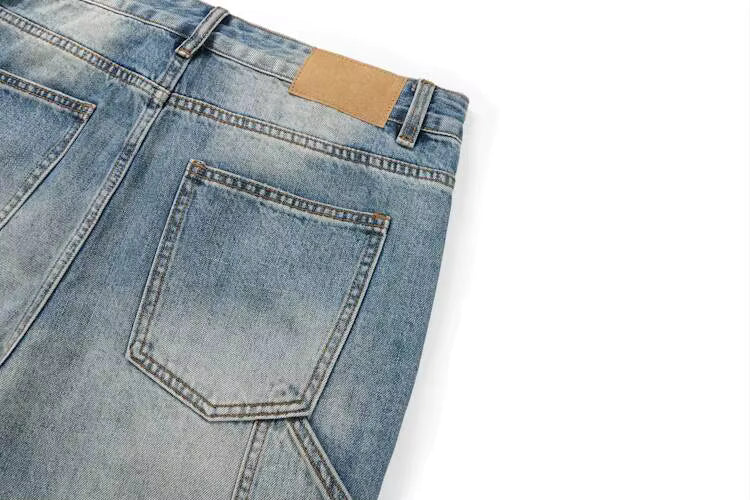 Close-up of the back waistband and pocket area of light blue denim jeans on a white background, showing a tan leather patch near the waistband.