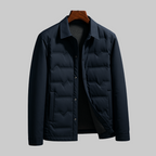 A men's dark navy quilted puffer jacket with a collar and snap-button front, displayed on a wooden hanger against a solid gray background.
