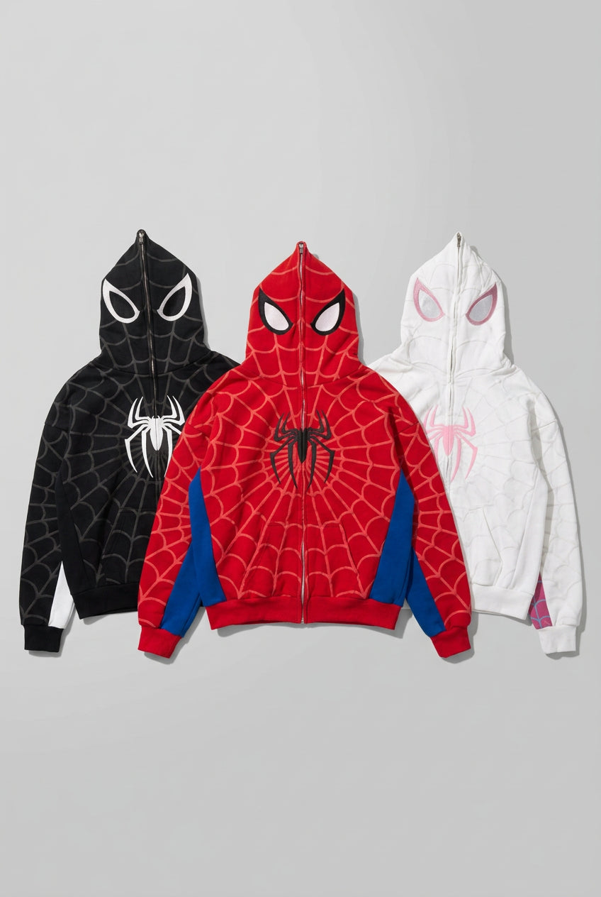 Three Spider-Man themed zip-up hoodies laid flat on a gray concrete floor. The front hoodie is red with blue side panels and a black spider logo on the chest.