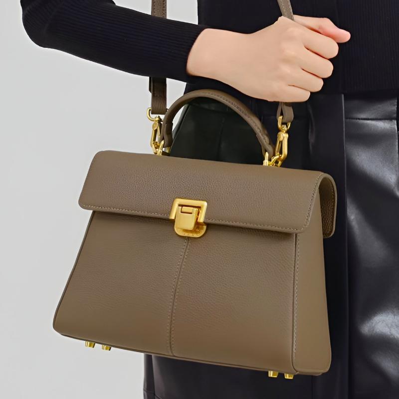 Brown handbag with gold accents held by a person against a neutral background
