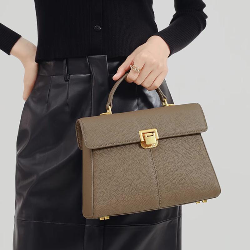 A taupe brown pebbled leather handbag with gold hardware, held by a model wearing a black top and black leather pants against a light gray background.