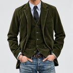 Man wearing a green corduroy jacket over a vest and shirt with a tie, on a plain background.