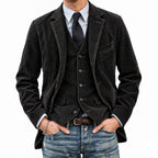 Man wearing a dark gray jacket over a vest and shirt with jeans on a light gray background