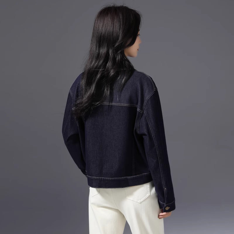A woman shown from the back wearing a dark navy denim jacket and white pants, photographed against a solid dark gray studio background.