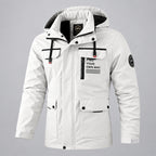 A men's hooded winter parka jacket in off-white with black trim, front zipper and snap closure, flap chest pockets, and printed text on the chest pocket reading 'FIND YOUR OWN WAY'. The jacket is shown against a blurred icy mountain background.