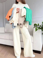 Person holding a stack of colorful sweaters in a living room setting