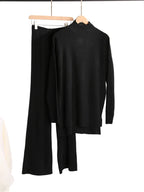 Black sweater and pants set on hangers against a white background